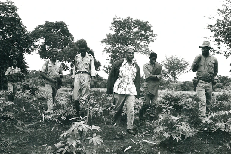 A man strides through croplands with four men walking behind him.