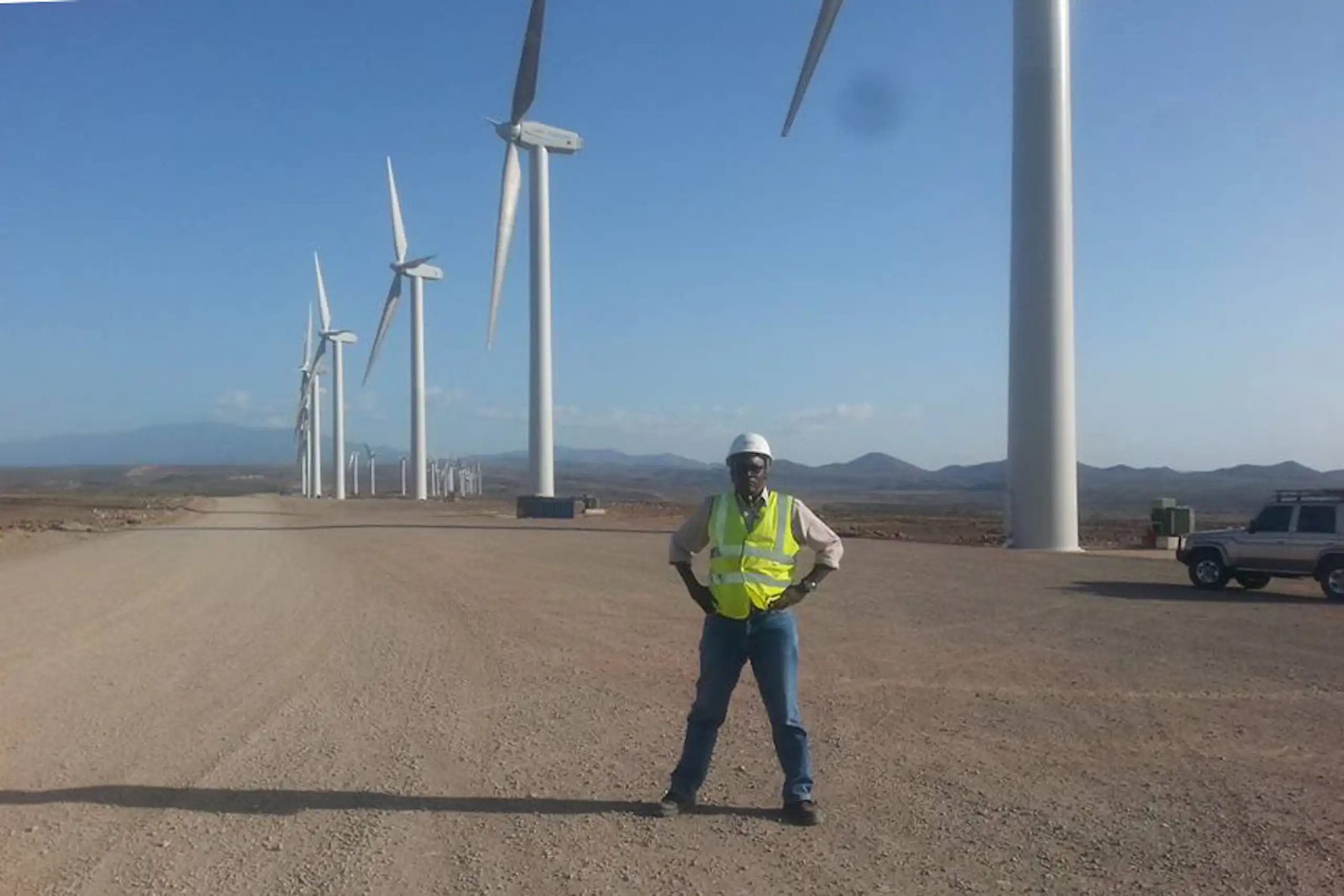 A man stands on a wide stretch of bulldozed land dotted by huge wind turbines