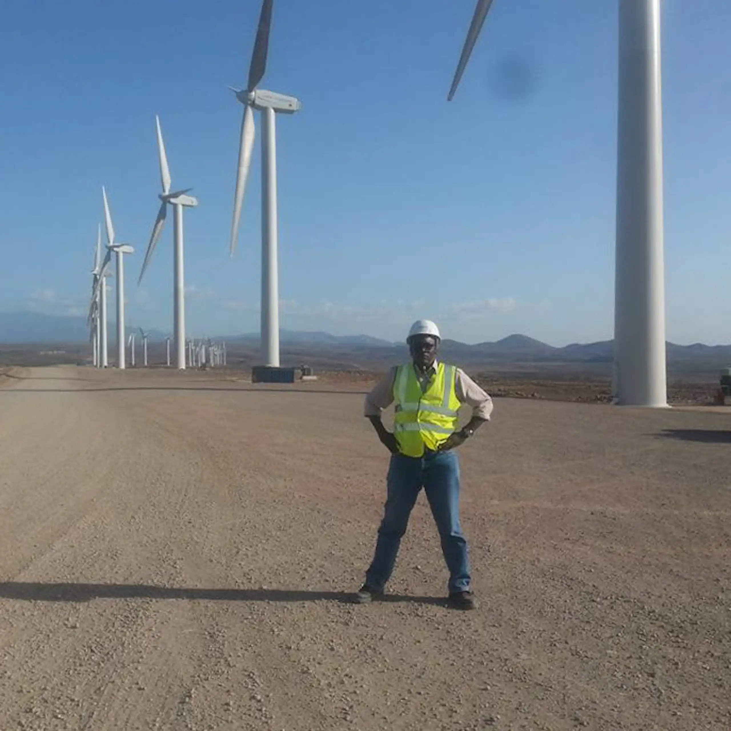 A man stands on a wide stretch of bulldozed land dotted by huge wind turbines