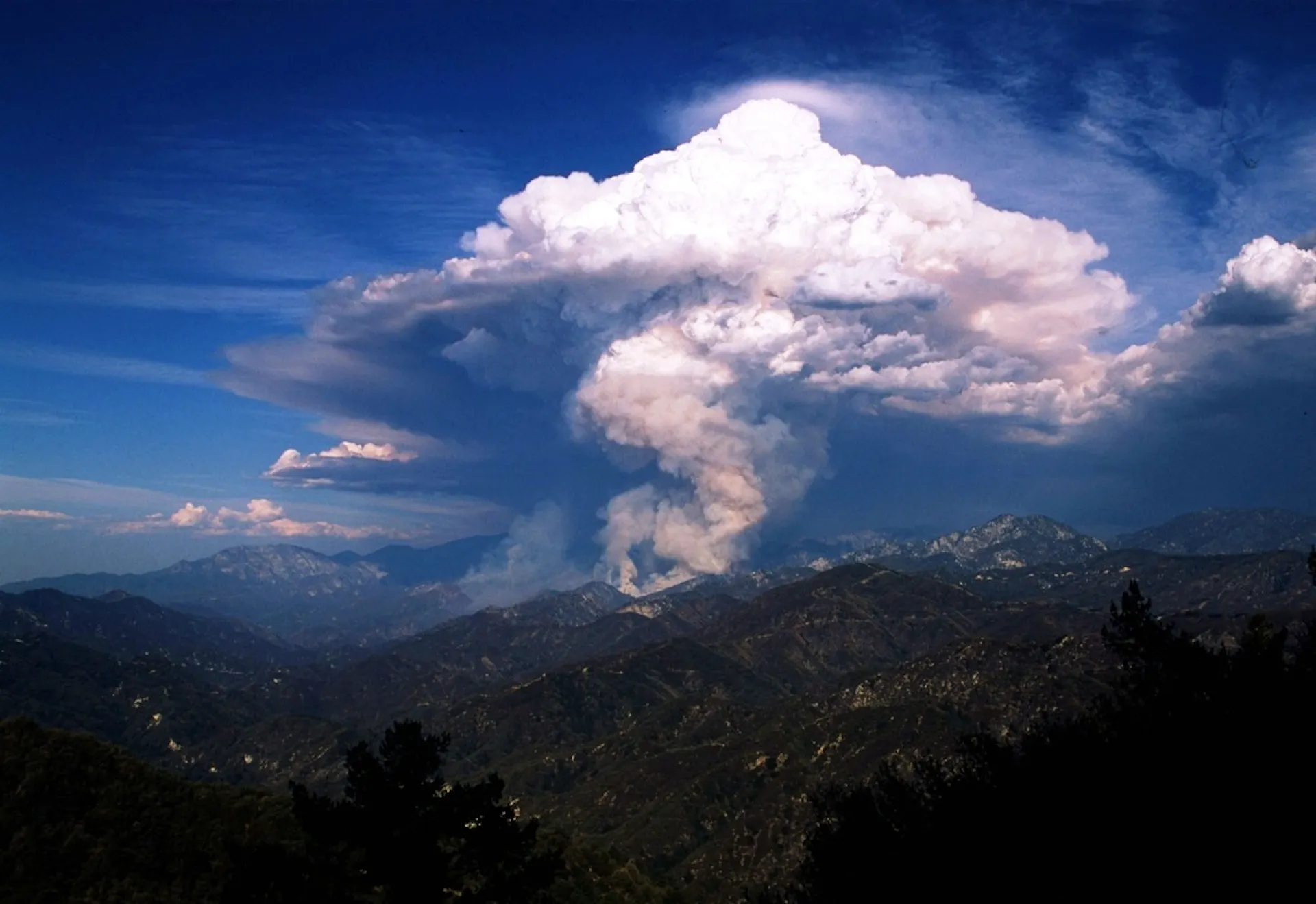 A large cloud looking like a thunderstorm rise above a canyon.