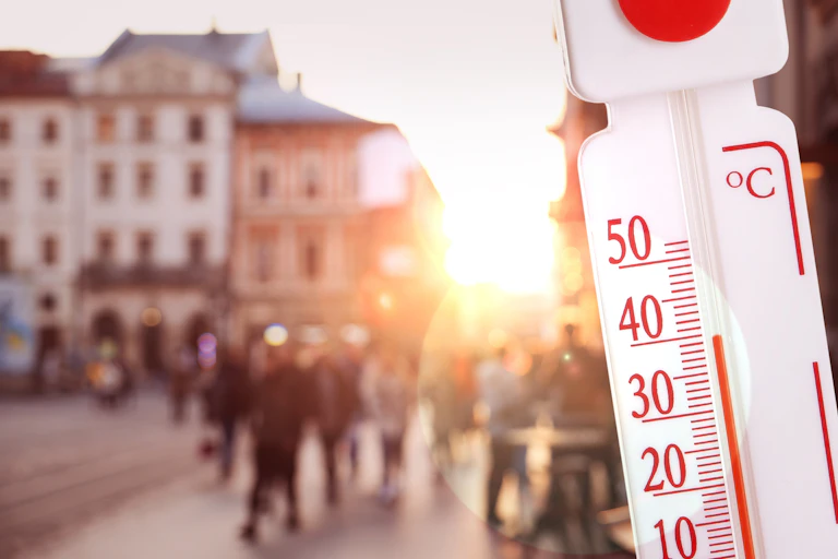thermometer with high temp, blurred city scene in background