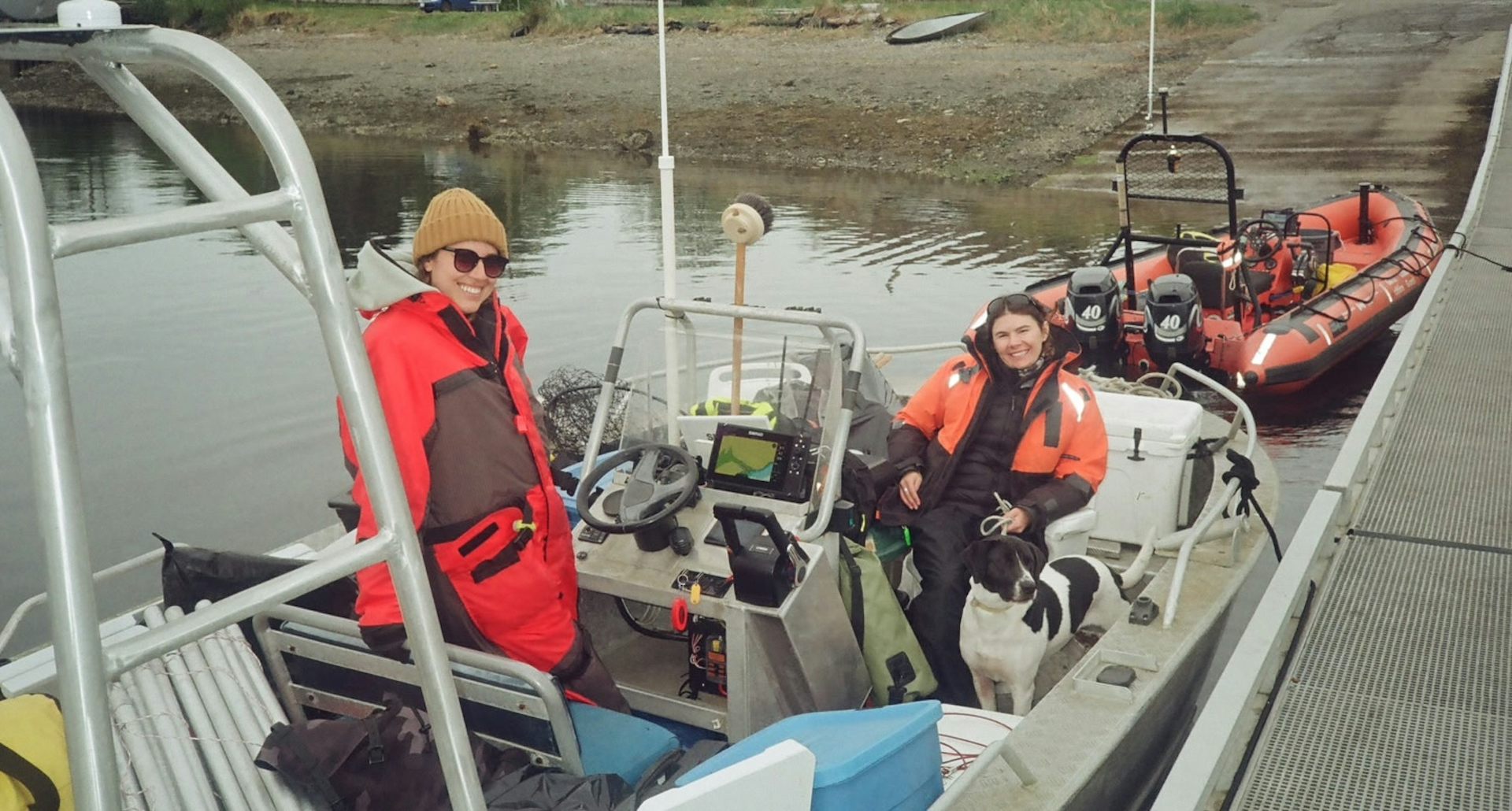 Two women in brightly coloured jackets and a dog aboard a small boat