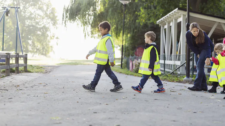 Children in safety vests walk to a playground.