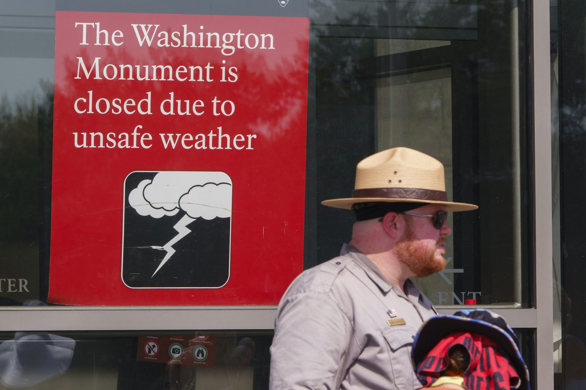 A ranger stands under a sign reading: The Washington Monument is closed due to unsafe weather.