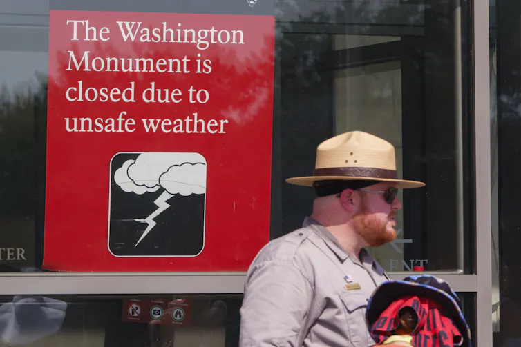 A ranger stands under a sign reading: The Washington Monument is closed due to unsafe weather.