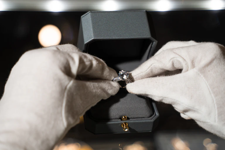 A jeweller holding an engagement ring with white gloves and placing it into a box