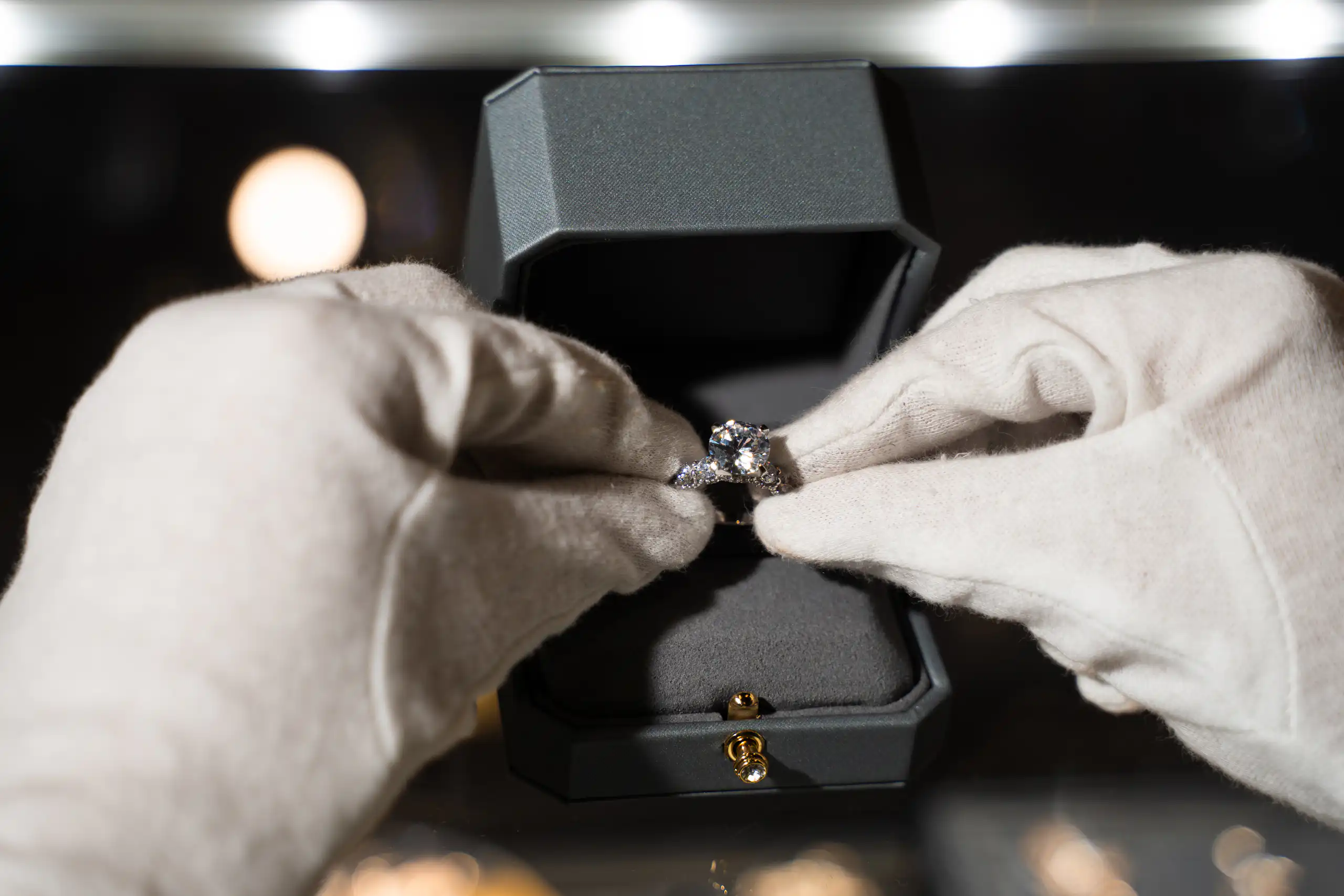 A jeweller holding an engagement ring with white gloves and placing it into a box