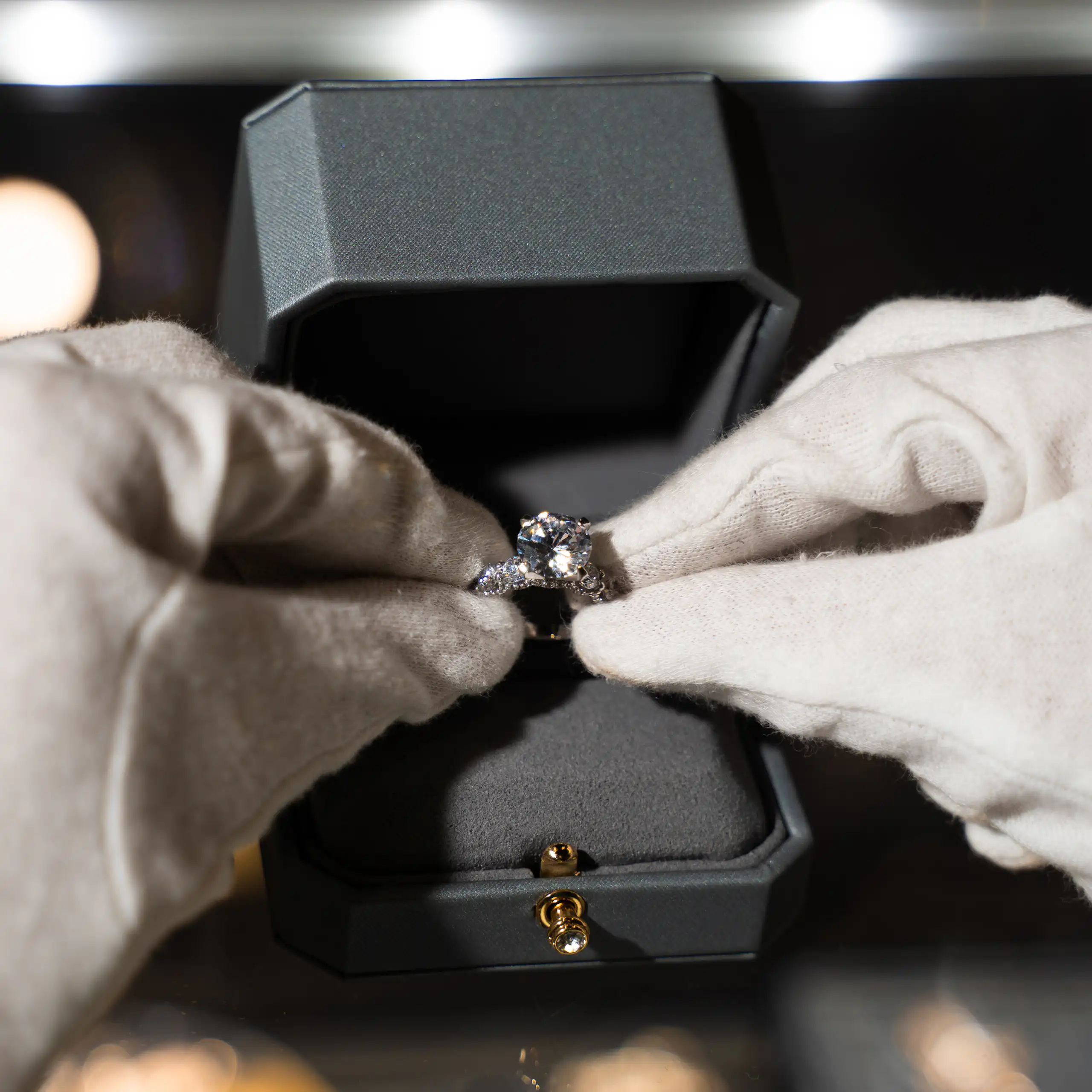 A jeweller holding an engagement ring with white gloves and placing it into a box