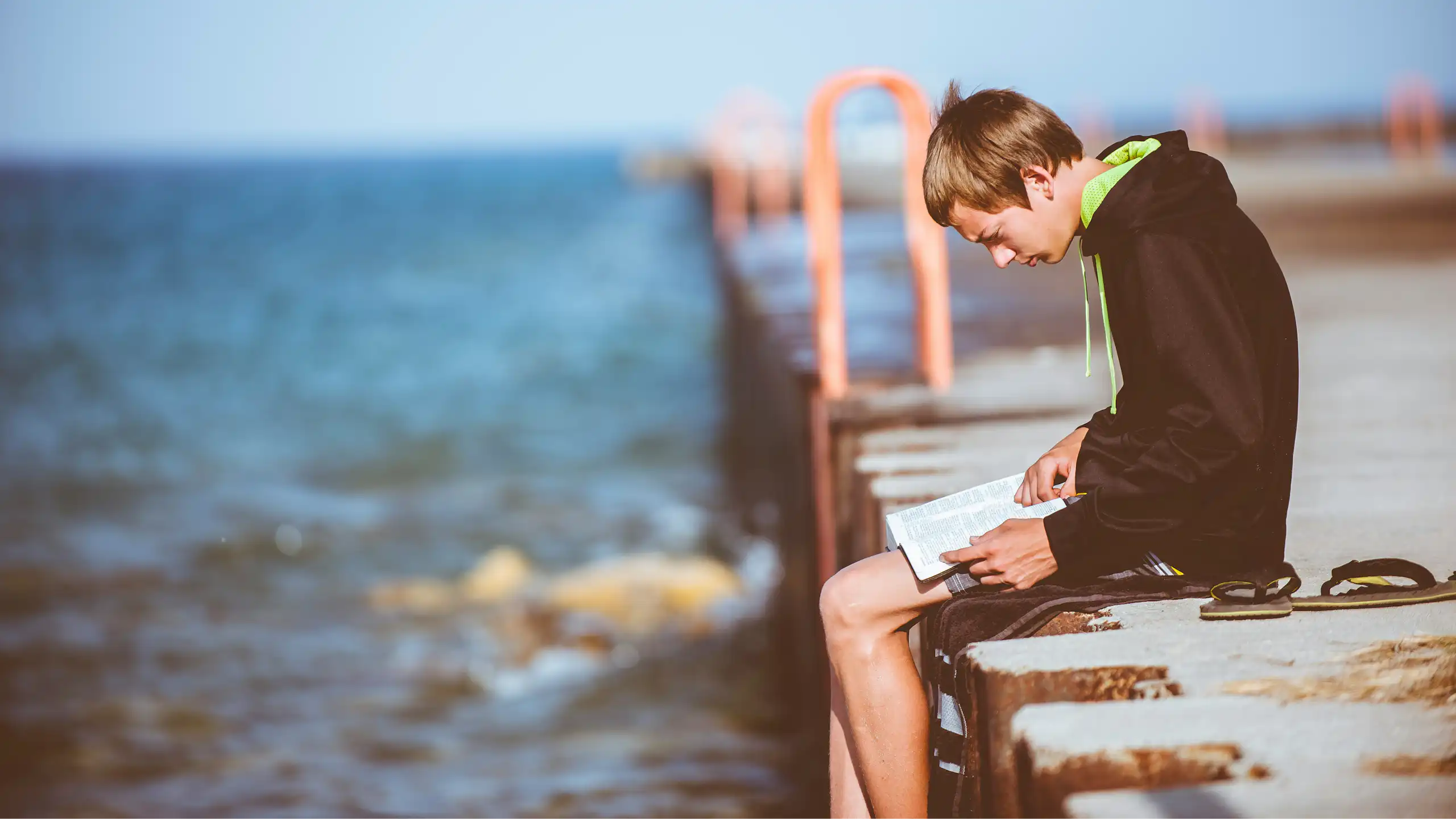 a boy reading on a pier over water