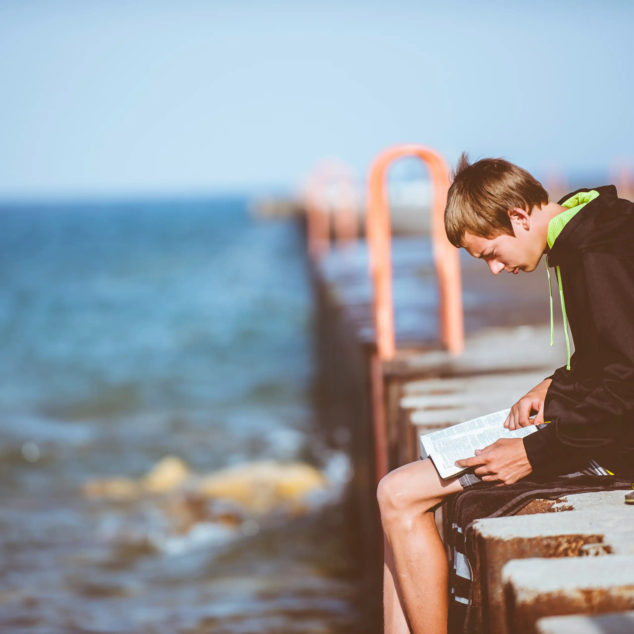 a boy reading on a pier over water