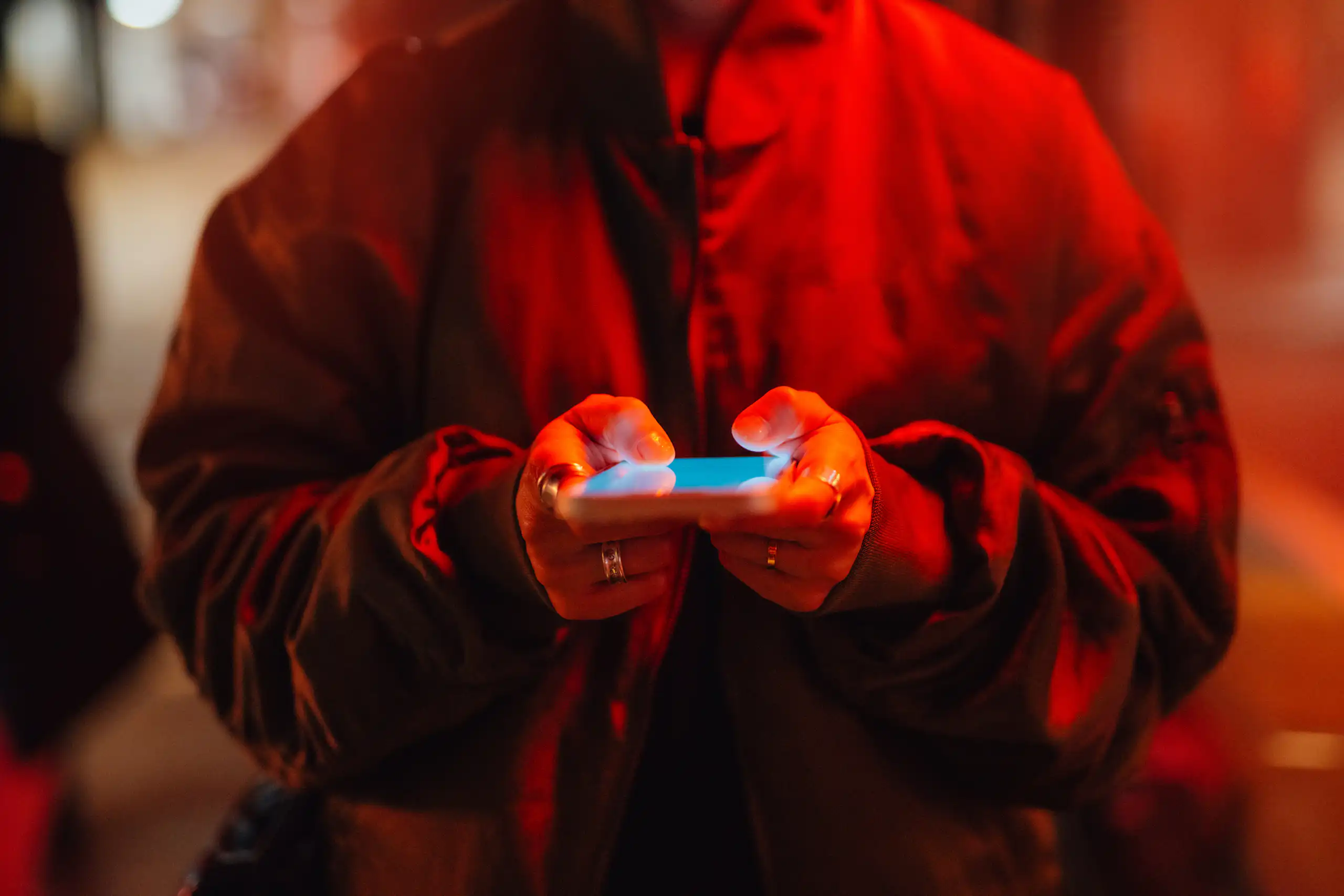 A person using a smartphone under red neon light.