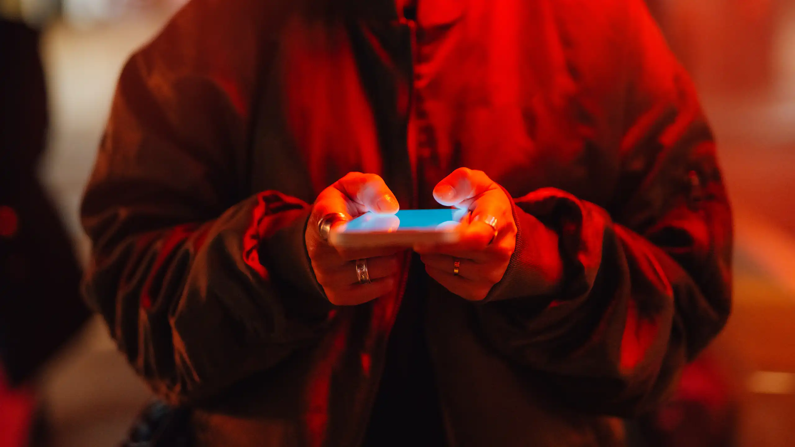 A person using a smartphone under red neon light.