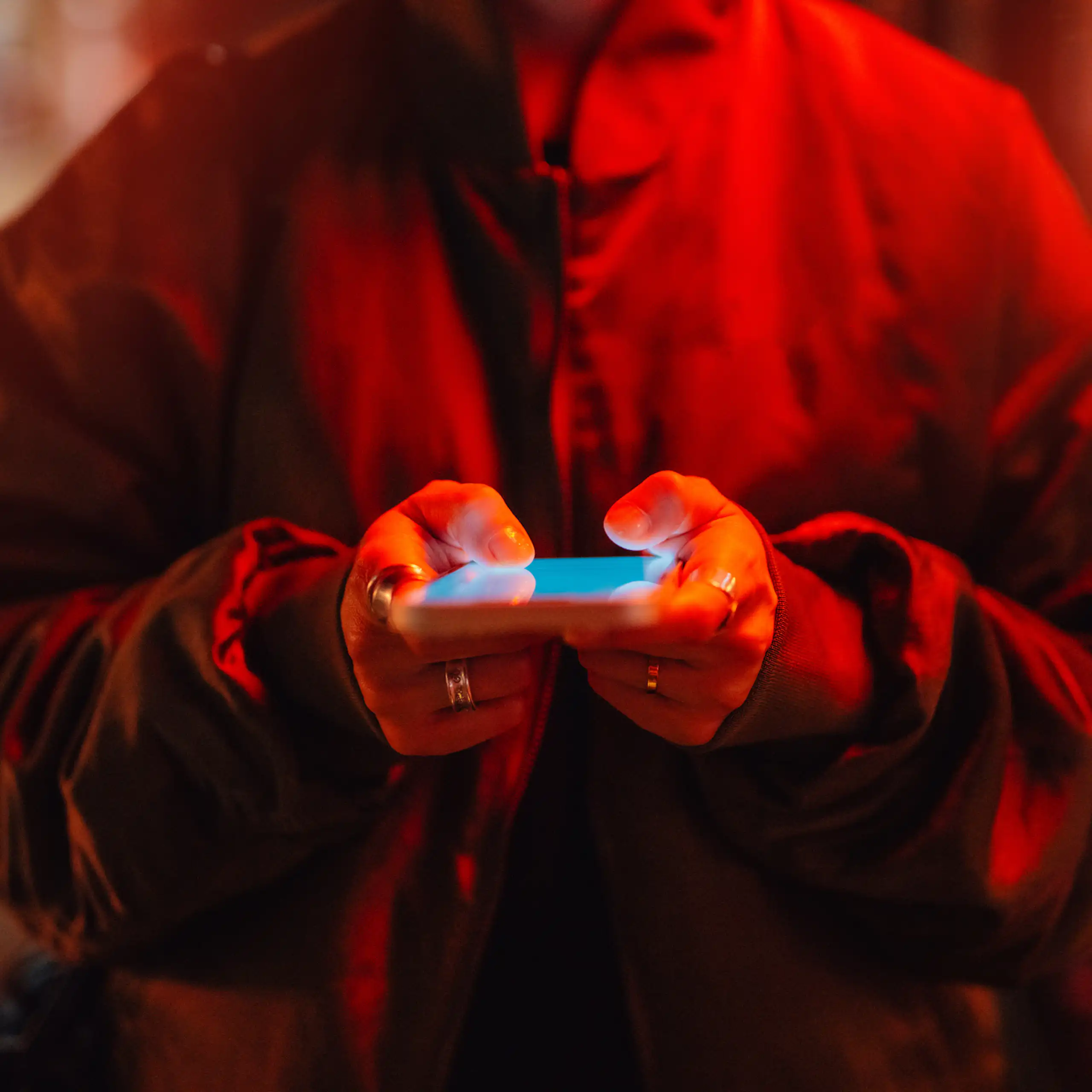A person using a smartphone under red neon light.