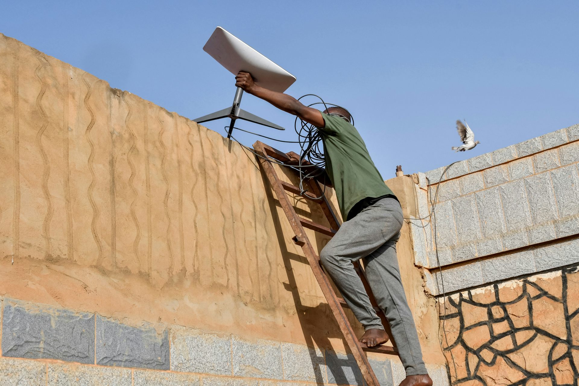 Un technicien installe une antenne parabolique au sommet d'un mur.