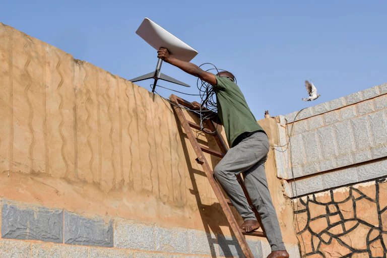 Un technicien installe une antenne parabolique au sommet d'un mur.