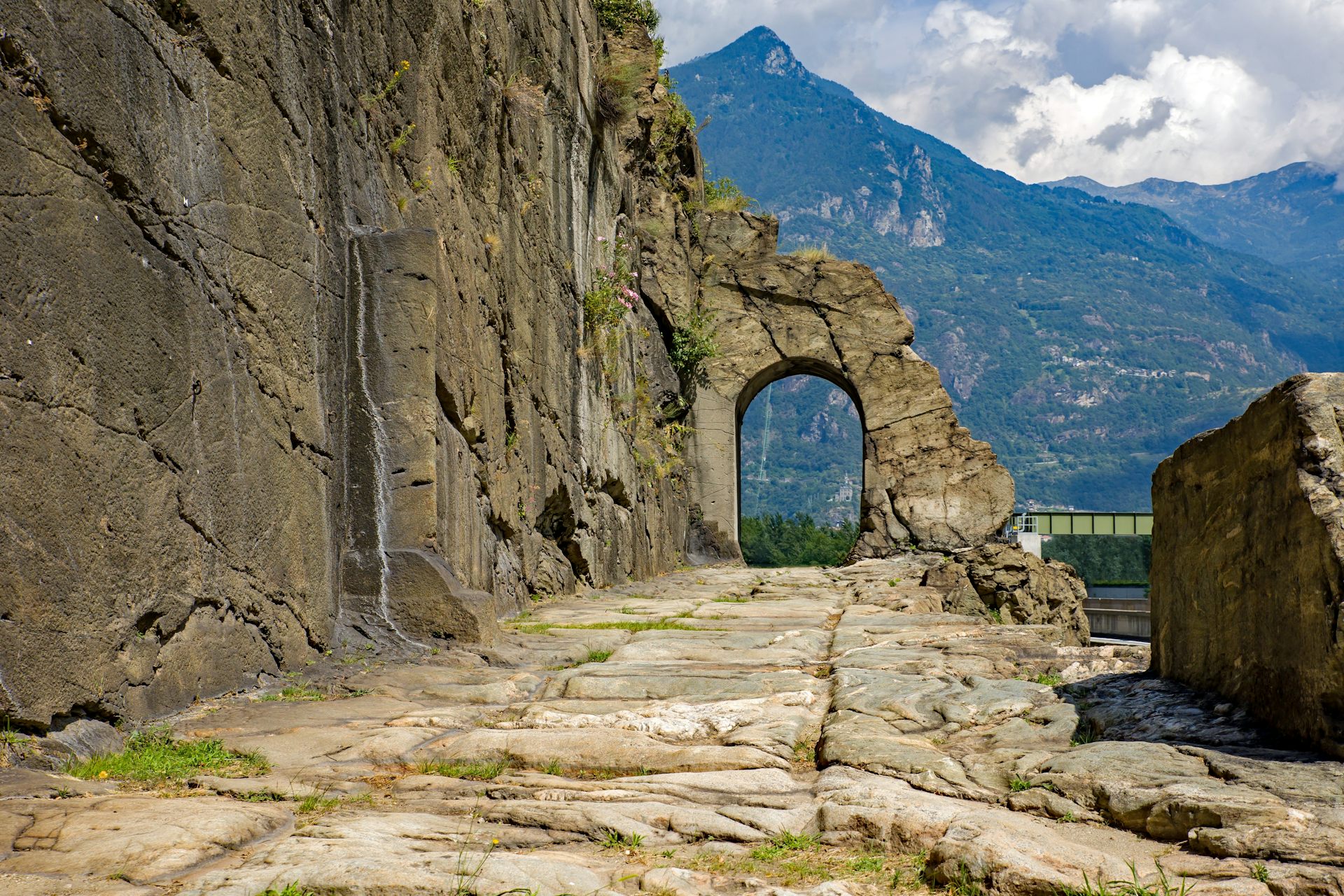 Un camí de pedra i un arc sobre ell, darrere dels quals es veu una muntanya.