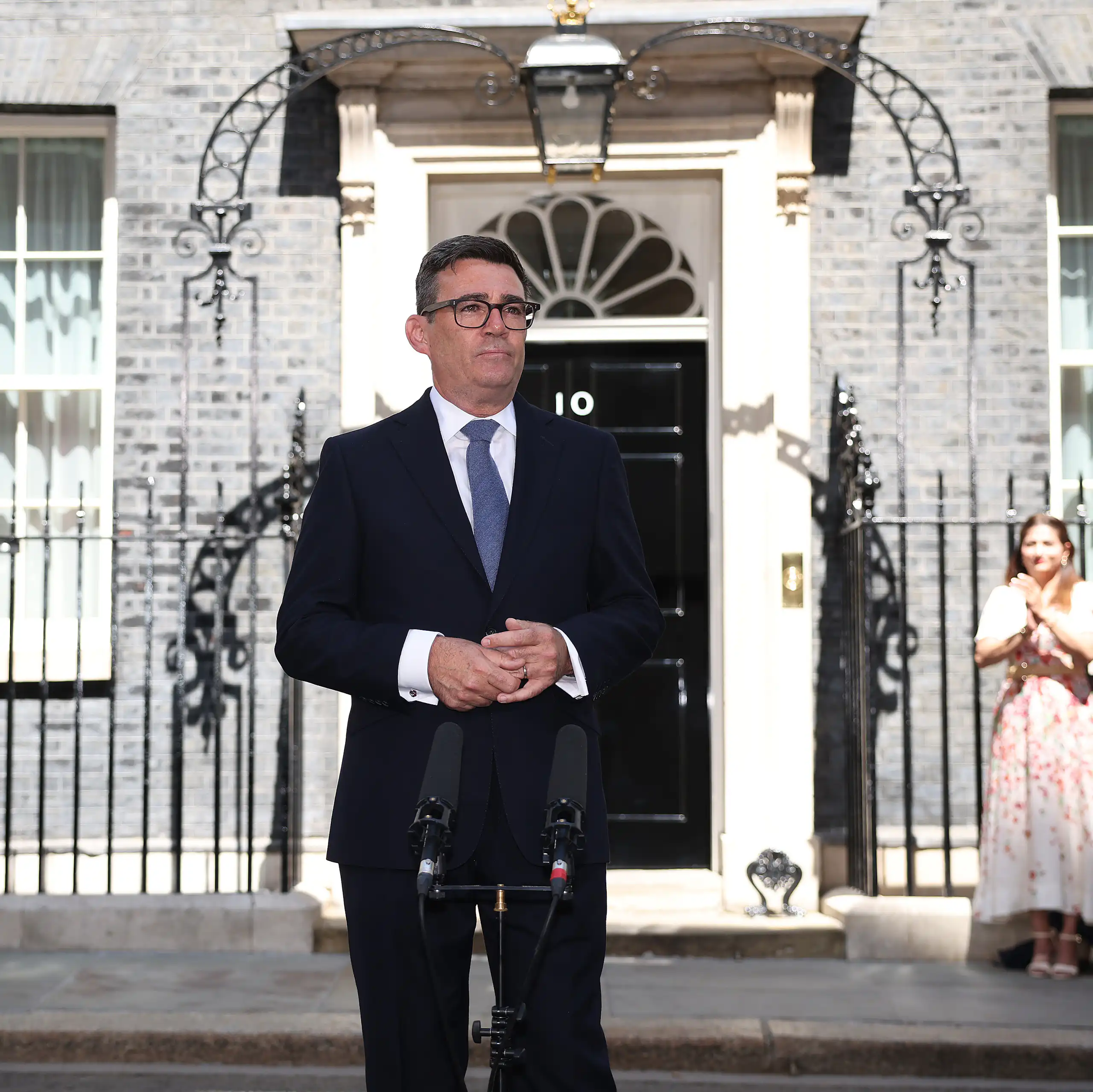A man in a suit stands in front of a black door.