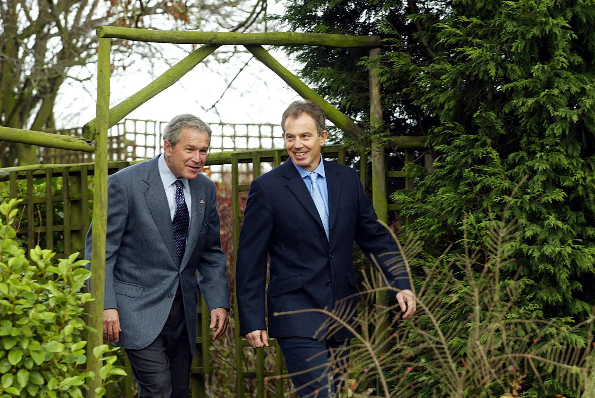 Two men walk under an archway.