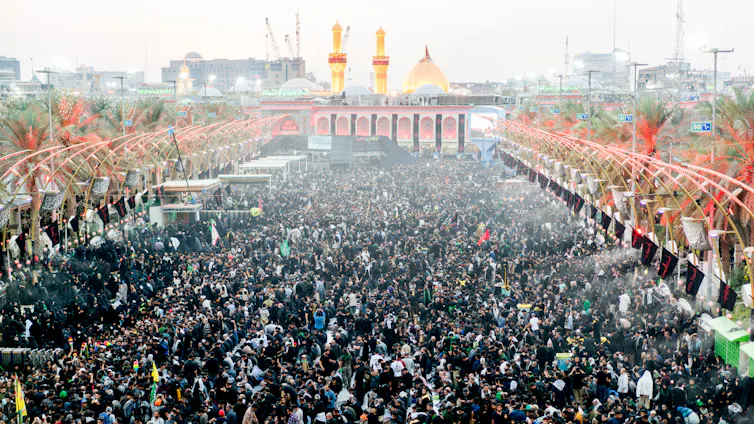 A large crowd of pilgrims gathered outside a shrine with a golden dome and two golden minarets.