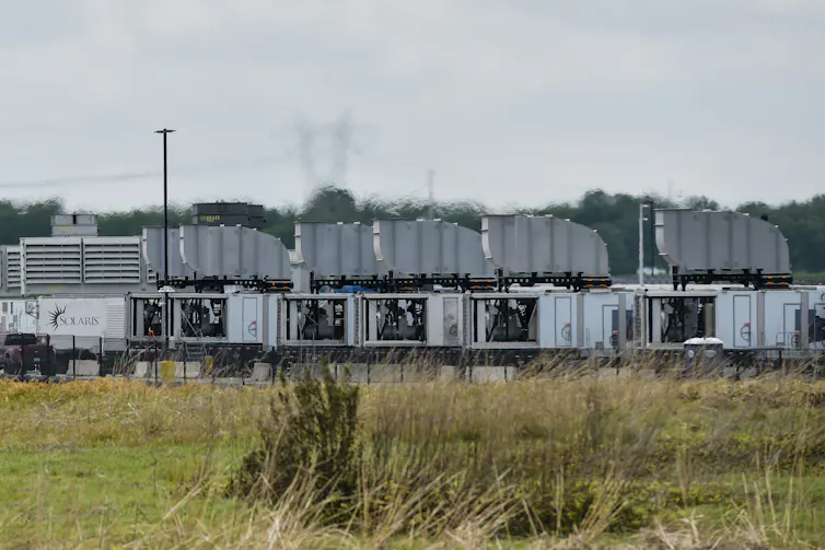 A view across a grassy area of large metal industrial boxes.