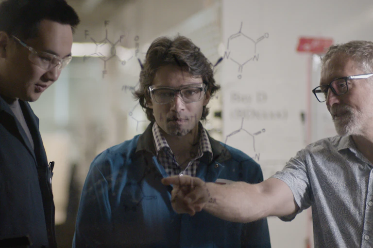 Three scientists discussing chemical drawings