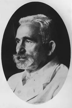 Black-and-white headshot of a bearded man in a white lab coat.