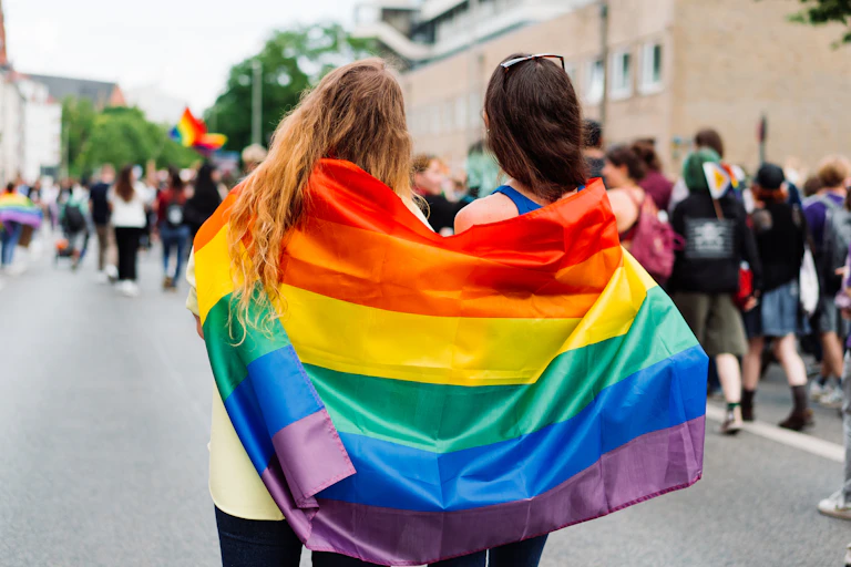 Two women wrapped in LGBTQI+ flag at rally, festival or pride event