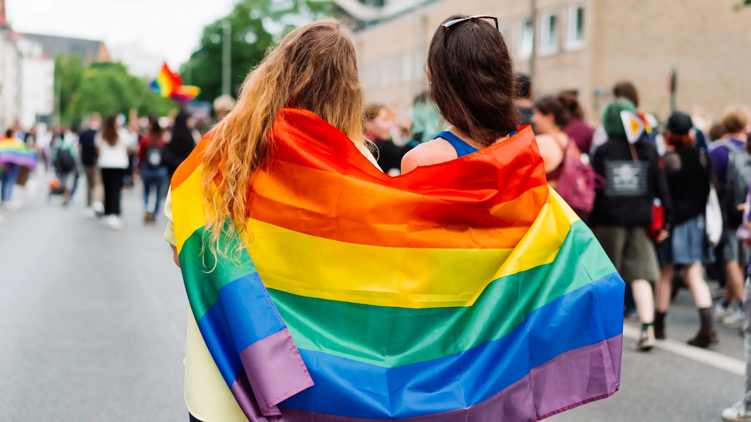 Two women wrapped in LGBTQI+ flag at rally, festival or pride event