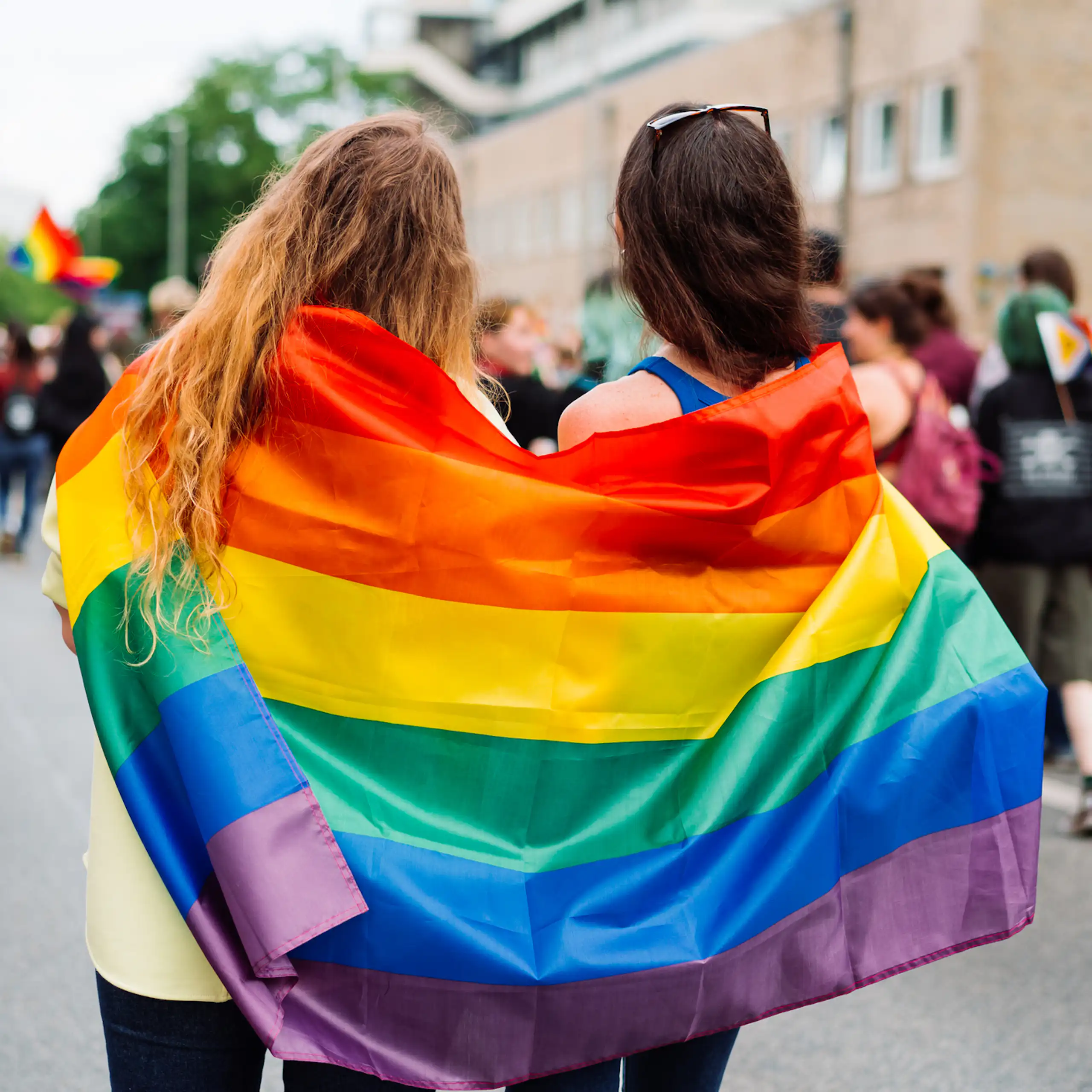 Two women wrapped in LGBTQI+ flag at rally, festival or pride event
