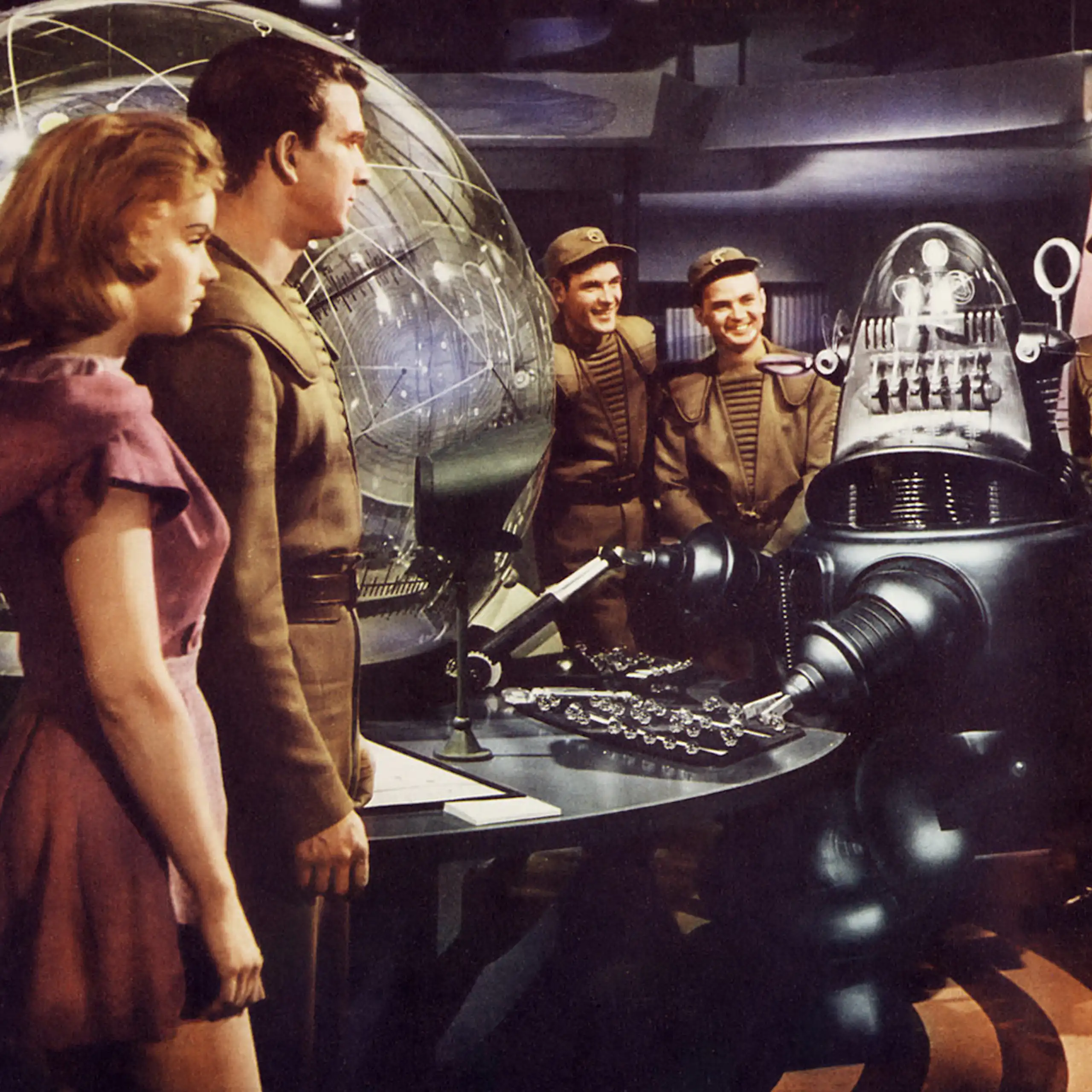 Film still: a woman, five men in uniform, and a robot on a space ship.