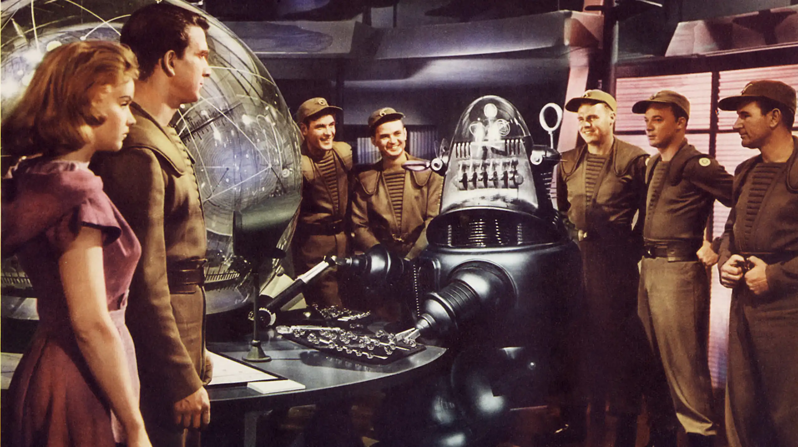 Film still: a woman, five men in uniform, and a robot on a space ship.