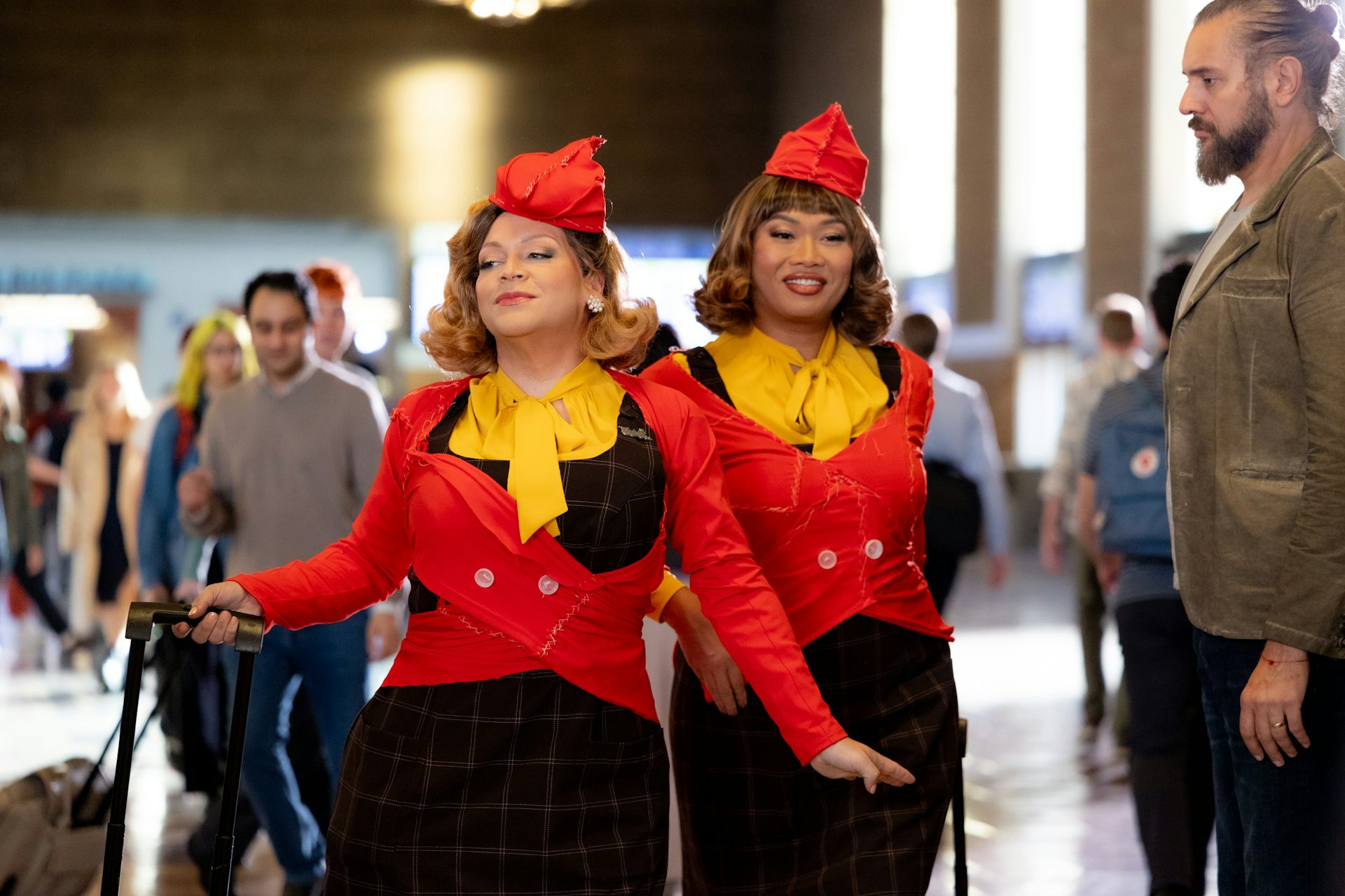 Two drag queens dressed as air hostesses in red and yellow uniforms.