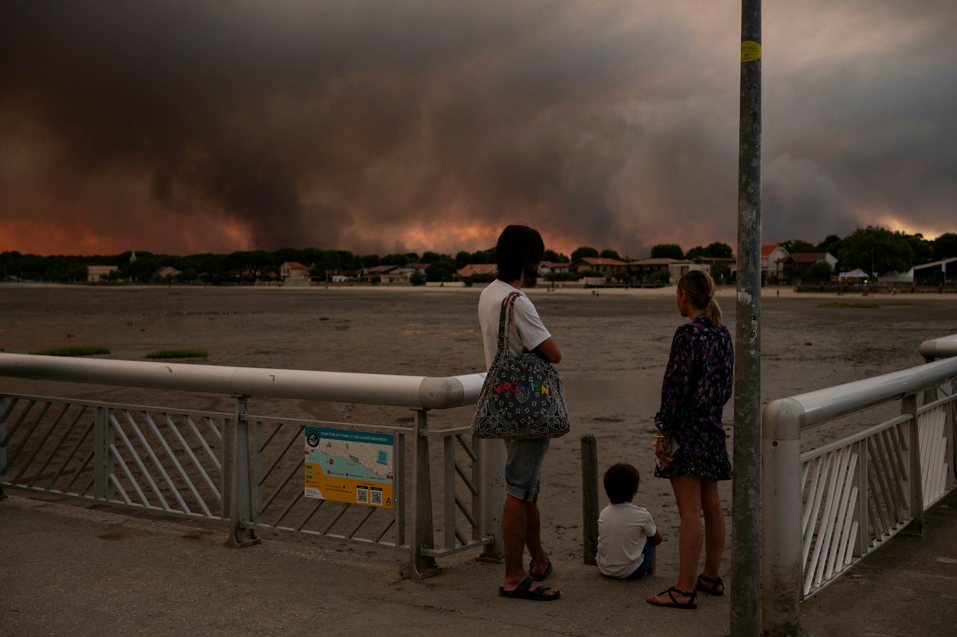 Deux adultes et un enfant regardant le panache de fumée de l'incendie 