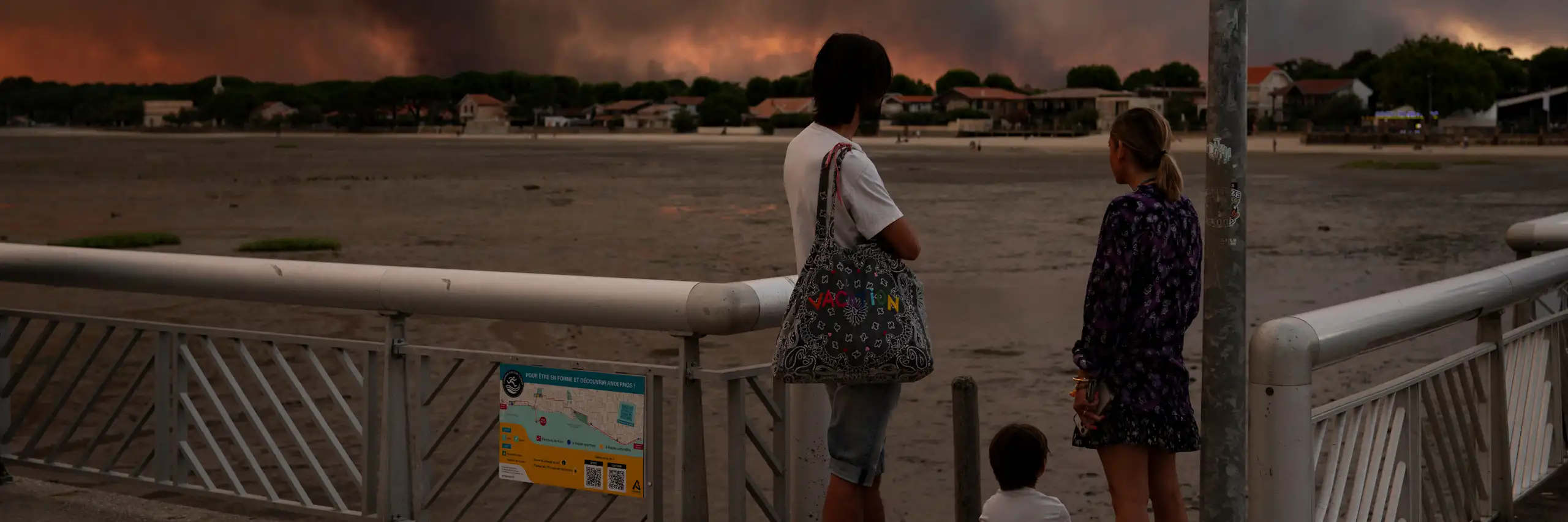 Deux adultes et un enfant regardant le panache de fumée de l'incendie