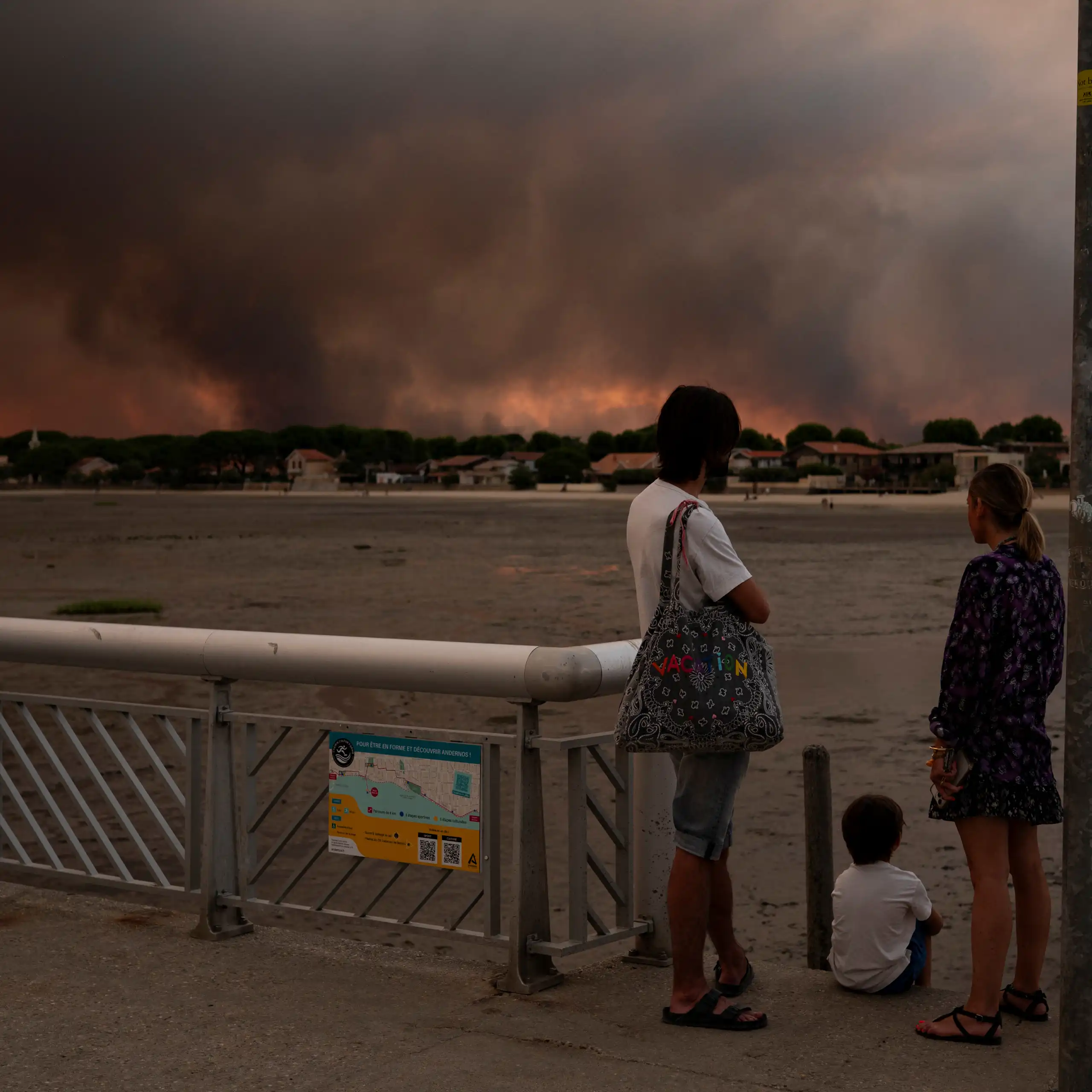 Deux adultes et un enfant regardant le panache de fumée de l'incendie