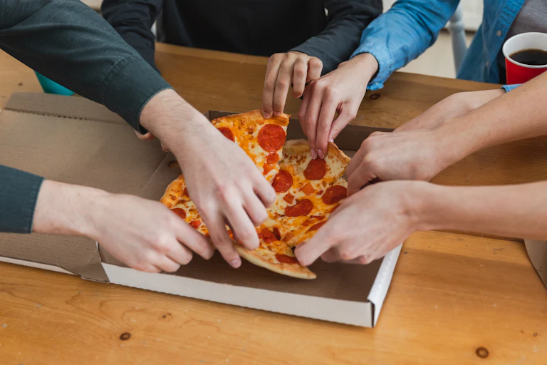 Manos cogiendo porciones de pizza.