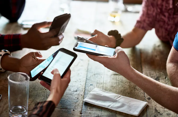 Close-up of group of people holding phones around a table