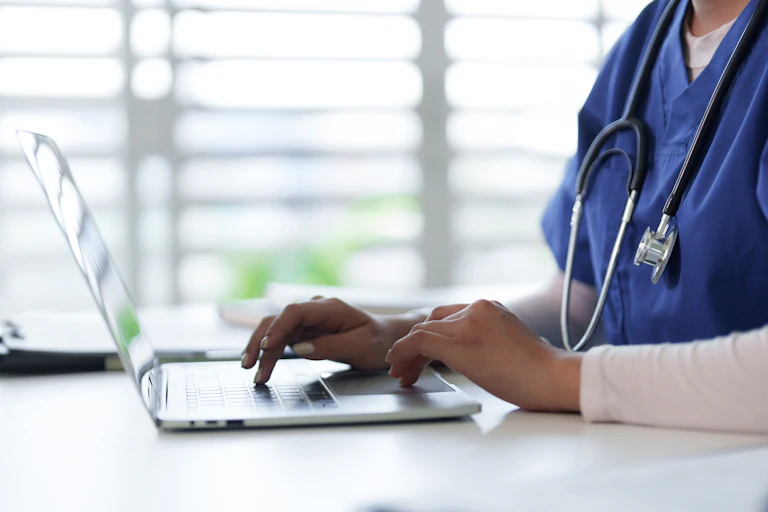 Person wearing scrubs and a stethoscope using a laptop