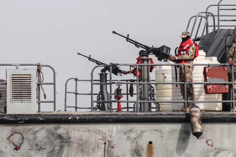 Men in army fatigues stand with large guns.