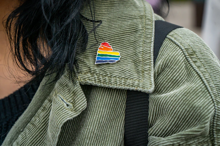 A close-up shot of a rainbow heart pin on the collar of somebody's green jacket.