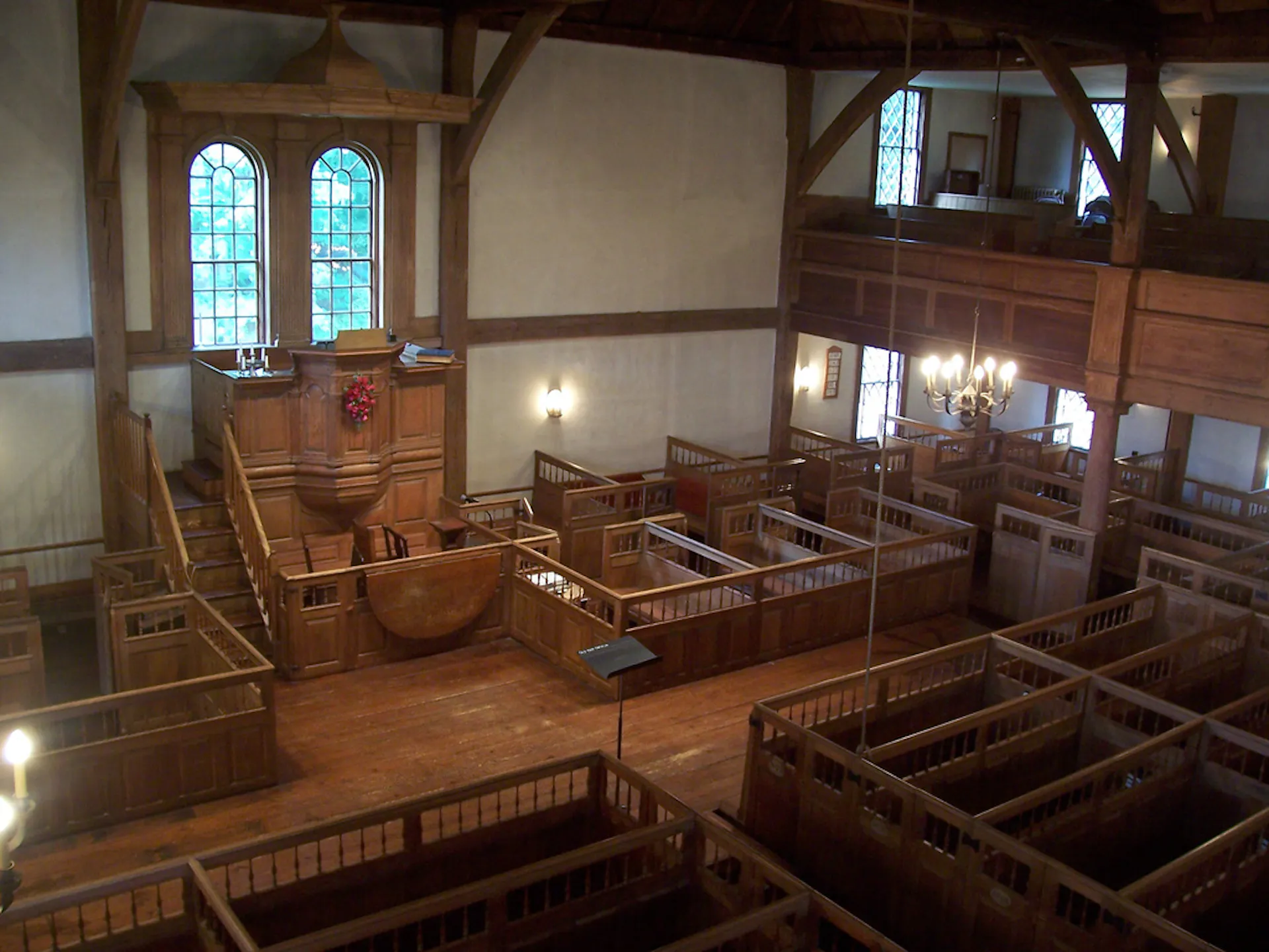 The interior of a plain church sanctuary whose wooden pews have tall sides.