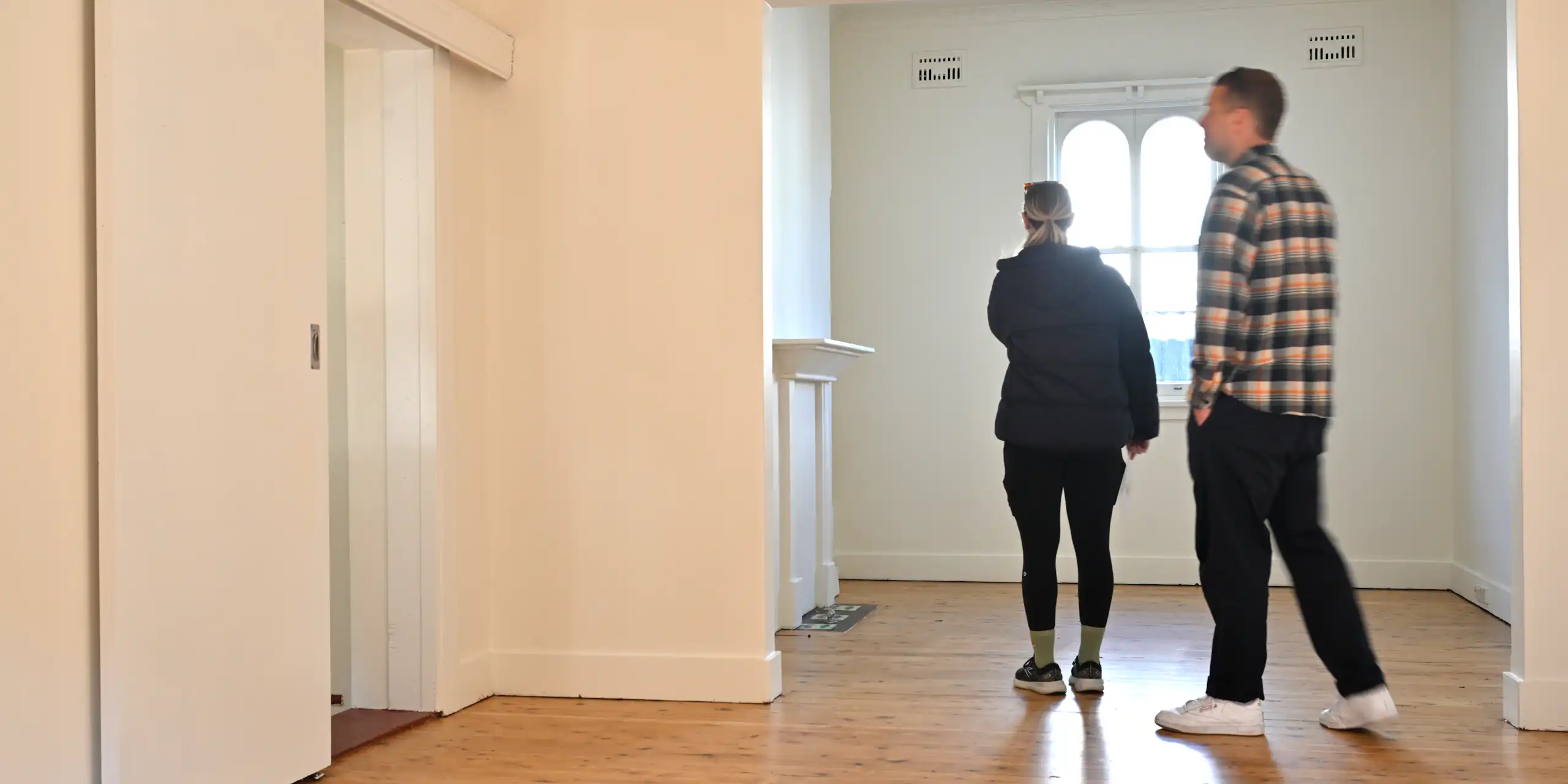 A young man and woman walk around an empty room with white walls