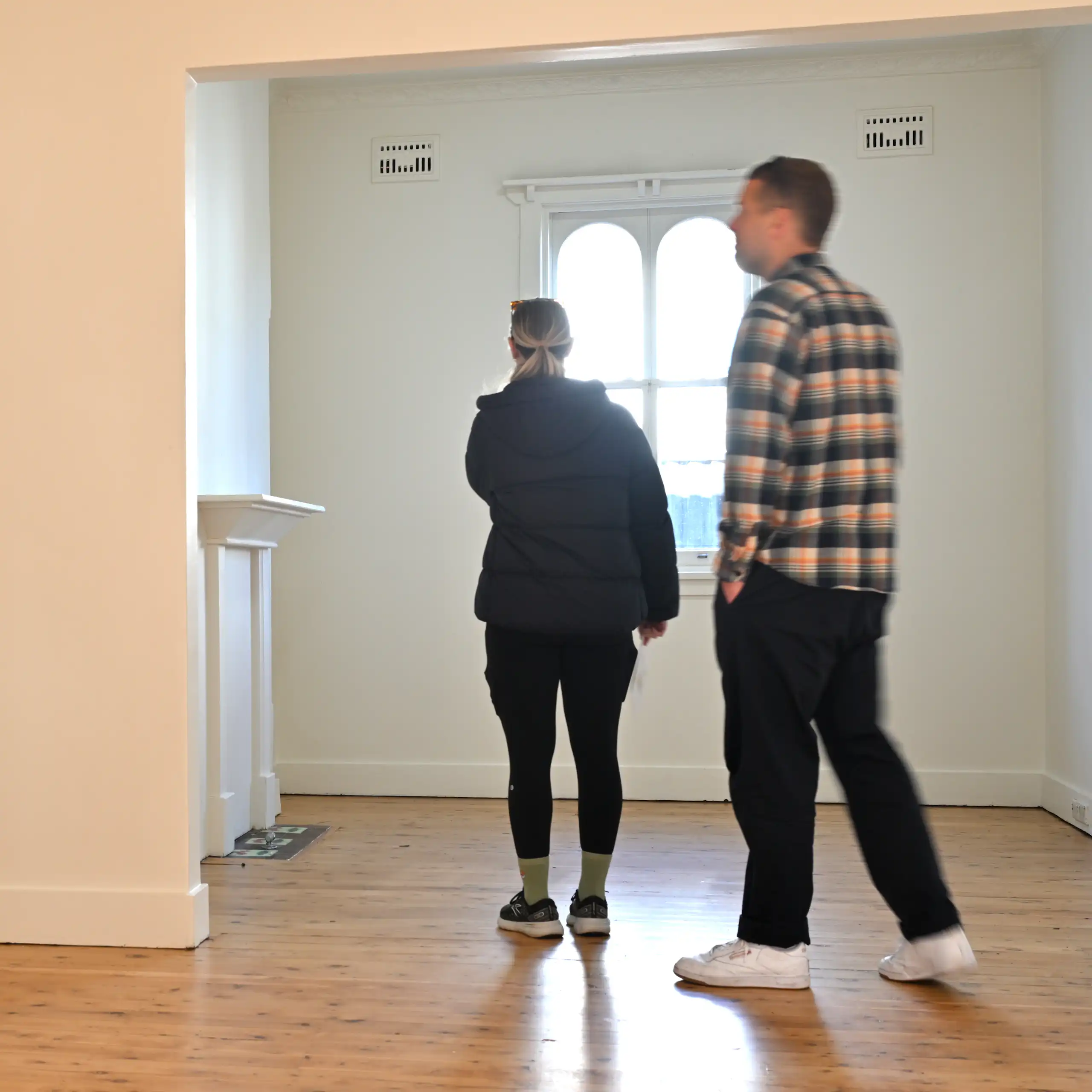 A young man and woman walk around an empty room with white walls