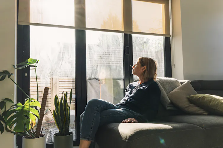 An women sits on a couch and basks in the sunlight.