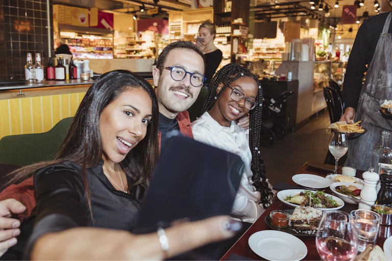 A group of three people take a selfie while having dinner.