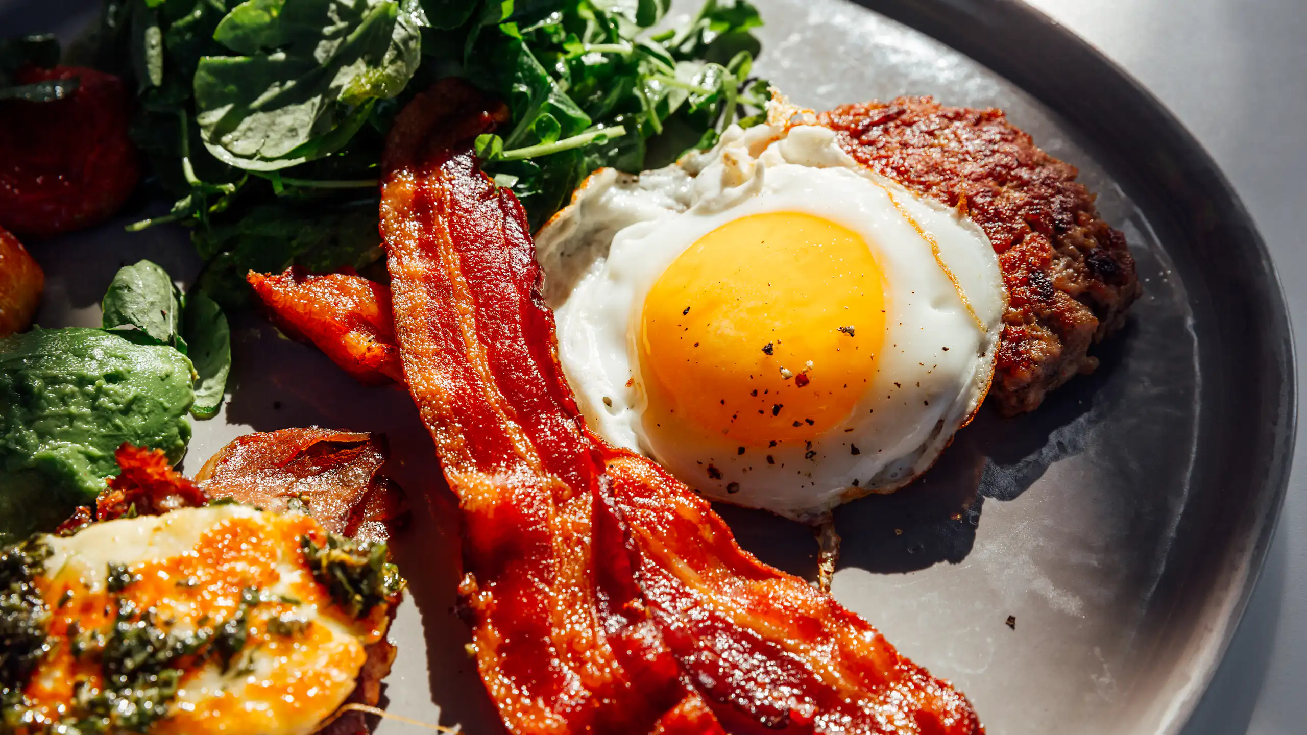 Plate of bacon, eggs, cheese and a beef patty.