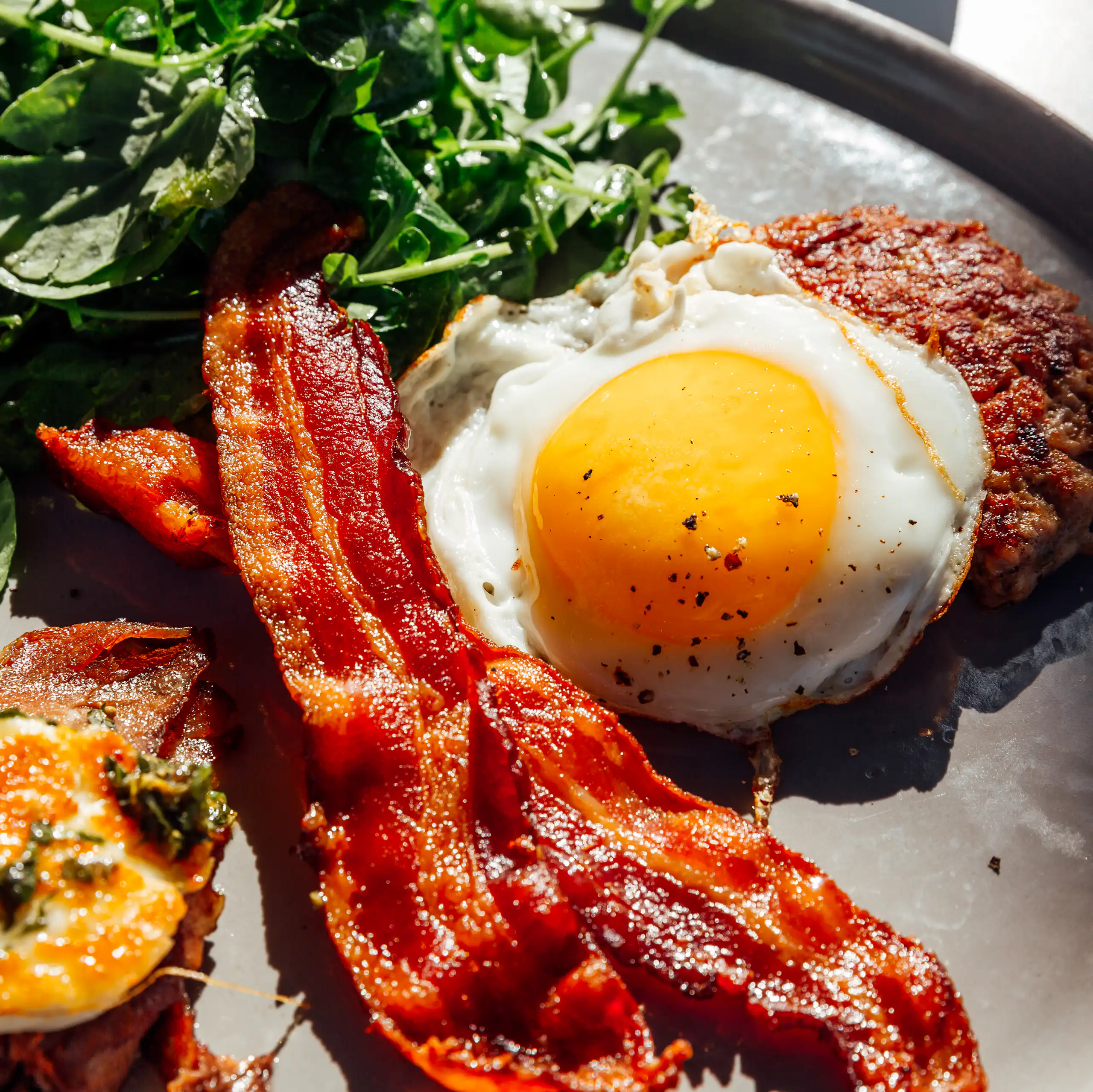 Plate of bacon, eggs, cheese and a beef patty.