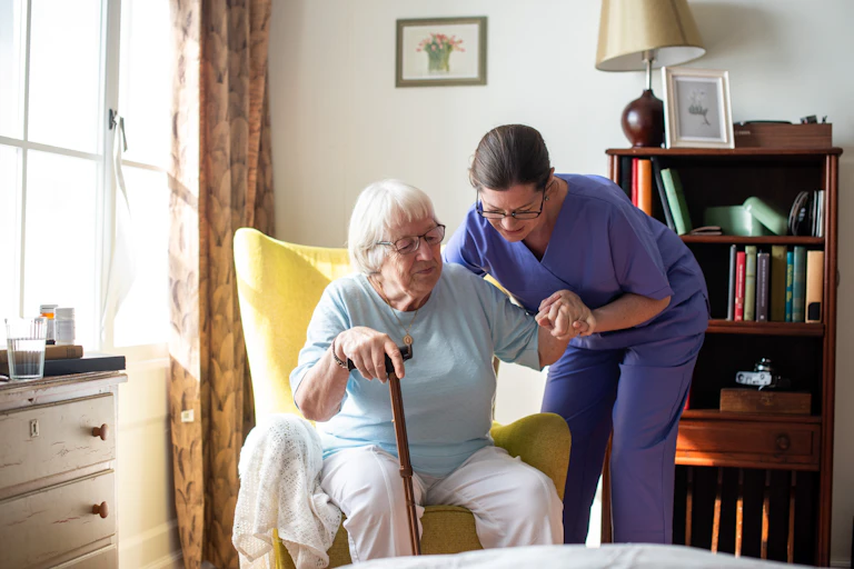 A care worker helping an elderly lady of her chair.