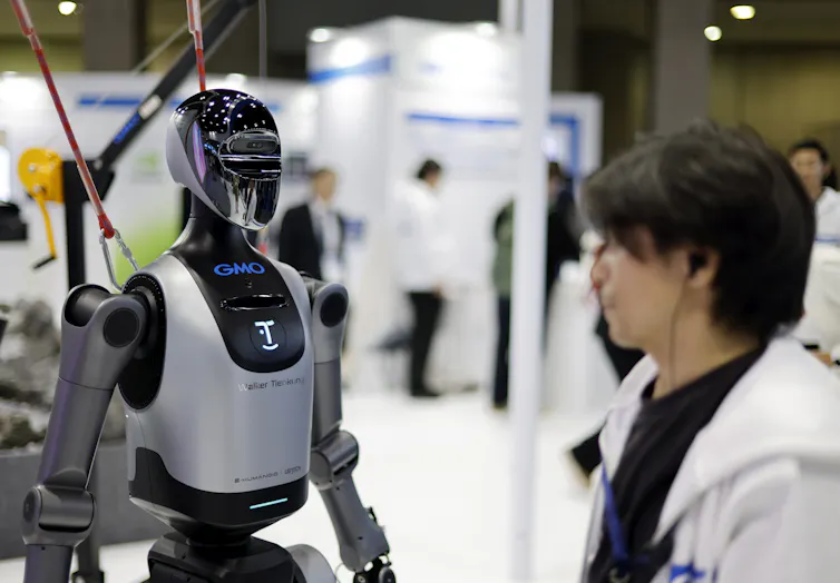 A staff member stands next to a humanoid robot during an exhibition in Tokyo.