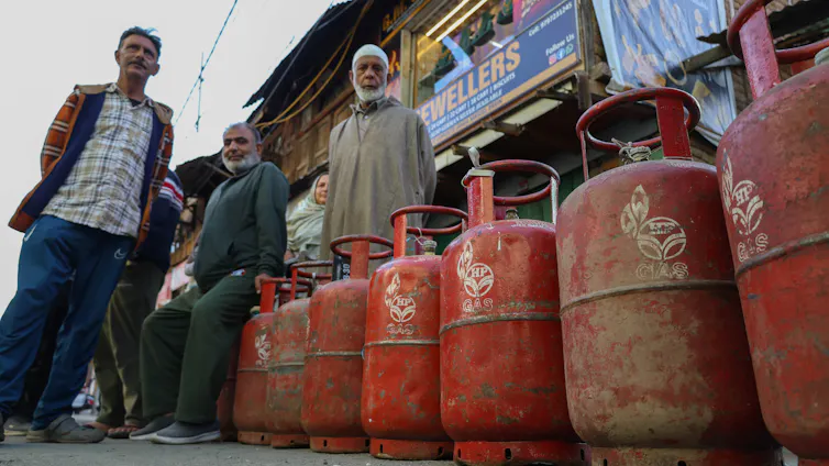 People stand on a street next to many metal cylinders.